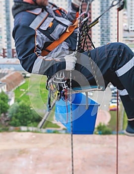 Professional climber rope access worker painting, repairing and cleaning windows on the facade of residential skyscraper high rise