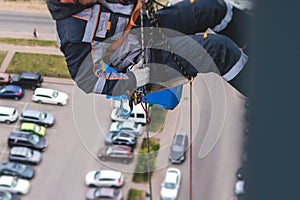 Professional climber rope access worker painting, repairing and cleaning windows on the facade of residential skyscraper high rise