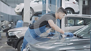 Professional concentrated auto mechanic checking car hood in auto repair shop. Side view of young Caucasian service man