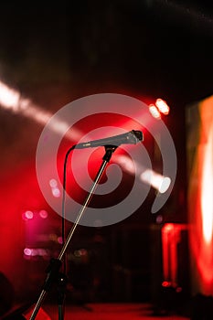 Professional condenser microphone resting on a stage, illuminated by a series of red stage lights