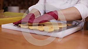 Professional confectioner in gloves puts a pieces of buscuit on a wooden board