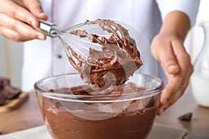 Professional confectioner whipping chocolate cream with balloon whisk at table, closeup