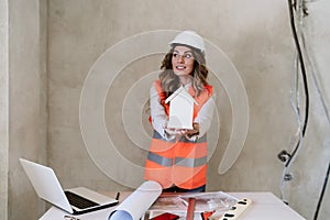 Professional confident architect woman in construction site holding house model. Home renovation