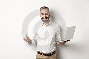 Professional confident businessman doing job on laptop, looking satisfied, standing over white background
