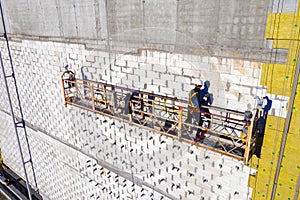 Professional construction Worker on scaffold elevator insulated wall facade with mineral wool. roofers wearing safety harness
