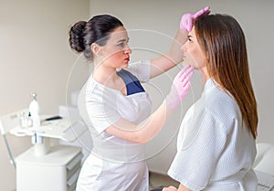 Professional cosmetician examining face skin of girl in clinic of esthetic cosmetology