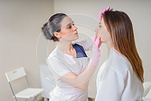 Professional cosmetician examining face skin of girl in clinic of esthetic cosmetology