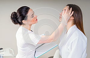 Professional cosmetician examining face skin of girl in clinic of esthetic cosmetology