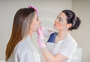 Professional cosmetician examining face skin of girl in clinic of esthetic cosmetology