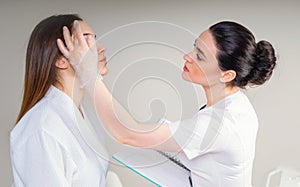 Professional cosmetician examining face skin of girl in clinic of esthetic cosmetology