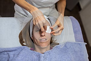 Professional cosmetician placing moisturizing pads on a young woman eyes