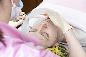 A professional cosmetologist applies a chemical peeling solution to the patient on the skin of the face with the help of hands in