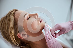 Professional cosmetologist injecting a dermal filler into the patient lips photo
