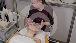 Professional cosmetologist woman doing facial massage to client of beauty salon.