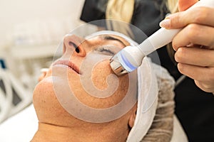 Professional cosmetology. Smart skilled cosmetologist using a modern device while doing hydrafacial procedure at a cosmetology