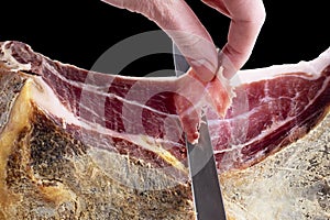 Professional cutter hand carving slices from a whole bone serrano jamon. Knife cutting a spanish serrano ham. Hands of a chef cutt