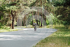 A professional cyclist man rides a bicycle outside the city on an asphalt road in the woods