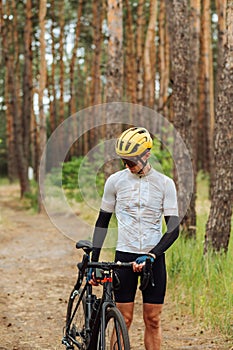 Professional cyclist in outfit walks with bike on forest path