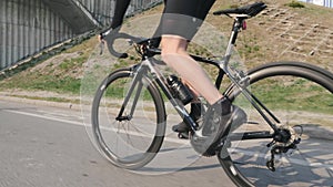 Professional cyclist riding bicycle out of the saddle. Side close up view of leg muscles in motion. Pedaling technique on bicycle.