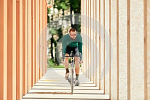 A professional cyclist in sportswear with glasses is preparing for a morning bike ride in a green city park. The concept