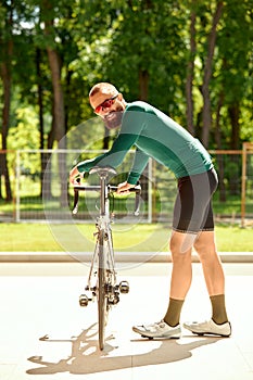 A professional cyclist in sportswear with glasses is preparing for a morning bike ride in a green city park. The concept