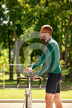 A professional cyclist in sportswear with glasses is preparing for a morning bike ride in a green city park. The concept