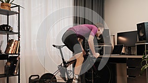 Professional cyclist is taking part in online cycling races on stationary bicycle. Man is cycling out of saddle on indoor smart bi