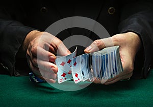 A professional dealer or croupier quickly shuffles playing cards in a club at a green table with playing chips. The concept of a