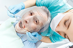 Professional dentist curing scared mature patient in dental clinic