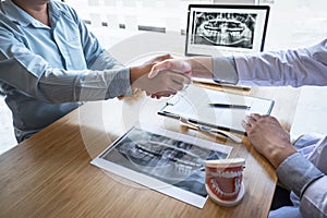 Professional Dentist showing jaw and teeth the x-ray photograph and shaking hands after finish discussing during explaining the photo