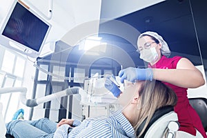 A professional dentist woman in glasses and overalls examines the oral cavity of a young girl in the dental chair using