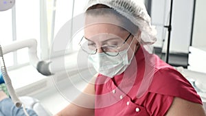 A professional dentist woman in glasses and overalls examines the oral cavity of a young girl in the dental chair using