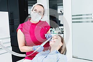 A professional dentist woman in glasses and overalls examines the oral cavity of a young girl in the dental chair using