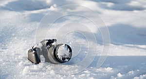 professional digital slr photo camera with frost lens lies in a snowdrift in winter in snow with copy space