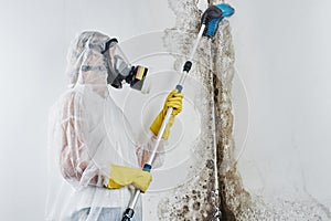 A professional disinfector in overalls processes the walls from mold with a brush. Removal of black fungus in the apartment and ho photo