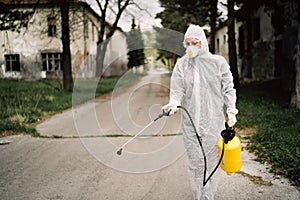 Professional disinfector in hazmat protection suit and N95 mask with chemical decontamination sprayer tank.Disinfecting streets photo