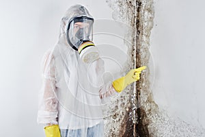 A professional disinfector in overalls and a mask points a finger at the black mold on the wall. Removal of the fungus in the apar photo