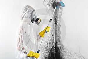 A professional disinfector in overalls processes the walls from mold with a brush. Removal of black fungus in the apartment and ho