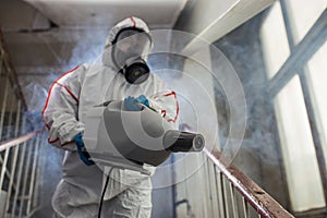 Disinfector wearing protective biological suit and gas-mask conduct disinfection photo