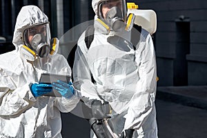 Professional disinfectors in protective hazmat suit walking through city streets