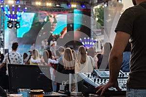 professional DJ music mixer, laptop at party festival with crowd of people in background, low light