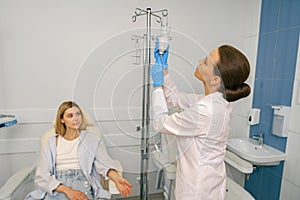 Professional doctor putting an IV drip to female patient intravenously in hospital ward