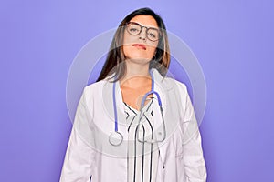 Professional doctor woman wearing stethoscope and medical coat over purple background Relaxed with serious expression on face