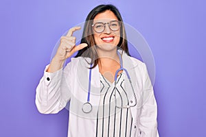 Professional doctor woman wearing stethoscope and medical coat over purple background smiling and confident gesturing with hand