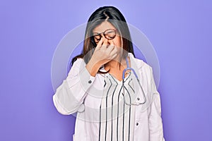 Professional doctor woman wearing stethoscope and medical coat over purple background tired rubbing nose and eyes feeling fatigue