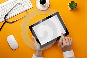 Professional doctor writing medical records in a digital tablet with stethoscope, keyboard, coffee cup and mouse