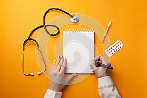 Professional doctor writing medical records in a notebook with stethoscope, syringe and pills