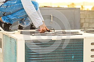 A professional electrician man is refiling the freon or gas into the heavy compressor of central air conditioning system by his