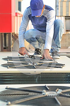 A professional electrician man is refiling the freon or gas into the heavy compressor of central air conditioning system by his