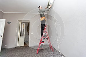 Professional electrician man with screwdriver maintaining, cleaning modern air conditioner indoors. Young technician